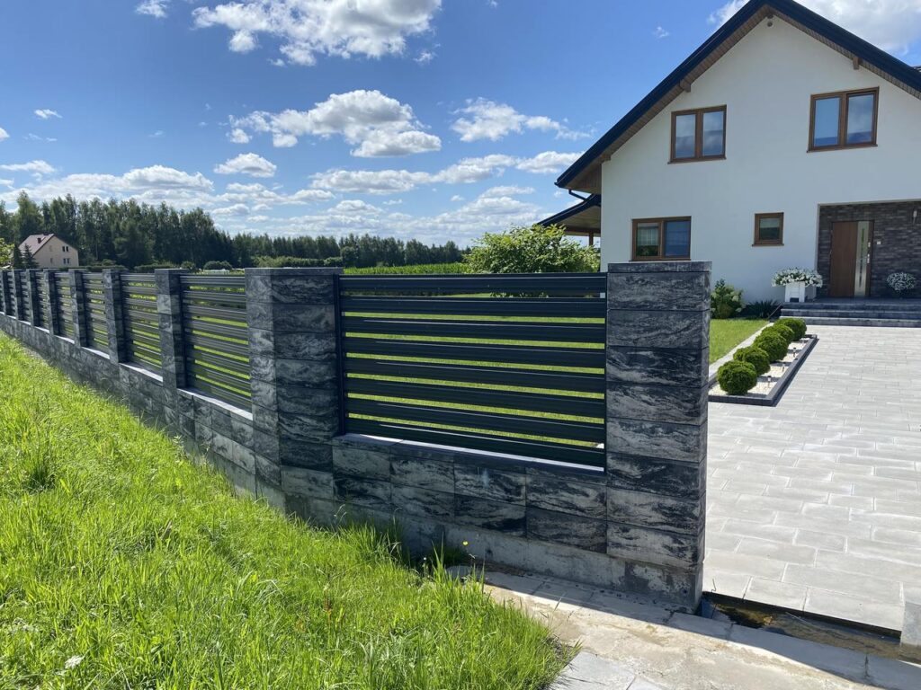 Pilka dekoratyvinė betoninė tvora su juodo metalo horizontaliais elementais Konekt tvoros sistemoje
